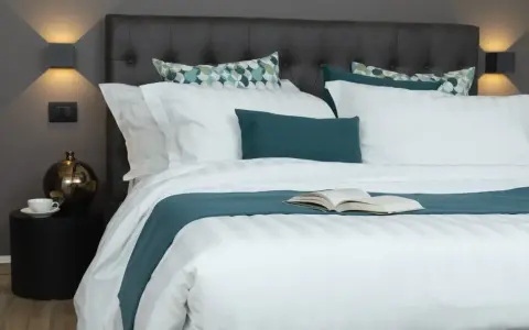 Letto con trapunta bianca a righe, cuscini coordinati e un libro aperto. Ecco come mettere la trapunta nel letto per un riposo perfetto.