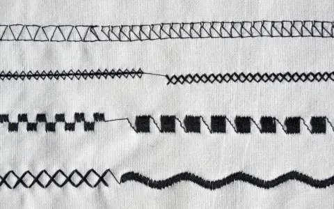 Close-up of various black sewing machine stitches on white fabric.
