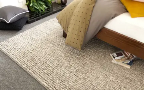 Un grande tappeto di lana intrecciata accanto a un letto. Scopri come lavare un tappeto di lana grande per mantenerlo come nuovo.