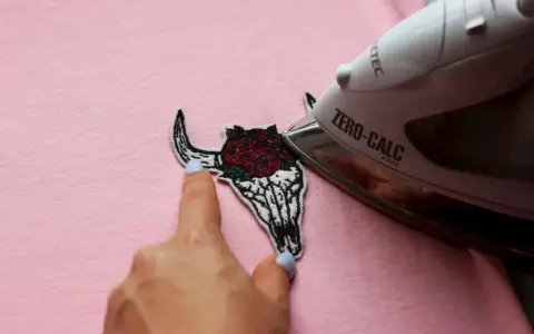 Come attaccare toppe termoadesive: un teschio di toro con rose viene stirato su una maglietta rosa.