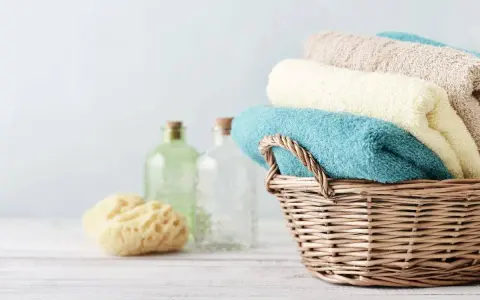 Cesto di vimini con asciugamani morbidi, come i rimedi della nonna. Accanto, spugna naturale e bottiglie di vetro.