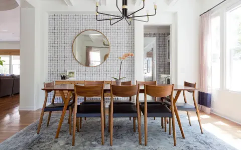 Tavolo da pranzo in legno con sedie in pelle nera, tappeto sotto il tavolo da pranzo si, con carta da parati a motivi geometrici e specchio rotondo.