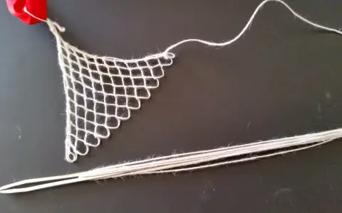 Un ago con filo bianco e un pezzo di rete a maglie, un tipo di ricamo eseguito su una rete a maglie, con un nastro rosso in alto.