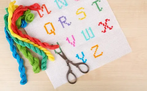 Fili colorati e forbicine pronti per ricamare nomi punto catenella su tela bianca con lettere dell'alfabeto.