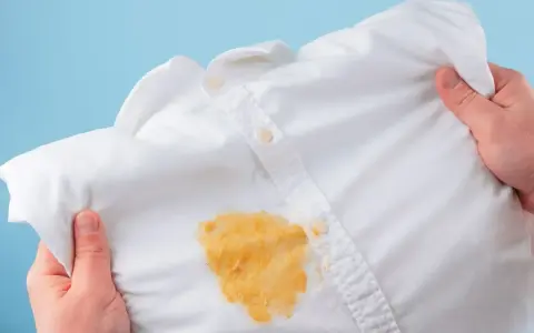 Come togliere le macchie gialle dalla biancheria colorata: una camicia bianca macchiata di giallo, tenuta in mano.
