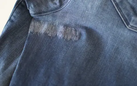 Dettaglio di un tessuto di jeans blu con un'area rattoppata con filo bianco, che mostra la cura nel rattoppare jeans.