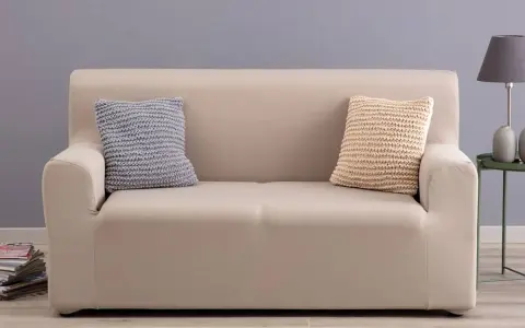 Divano con copridivano in tessuto color crema, due cuscini decorativi a maglia, uno grigio e uno beige.