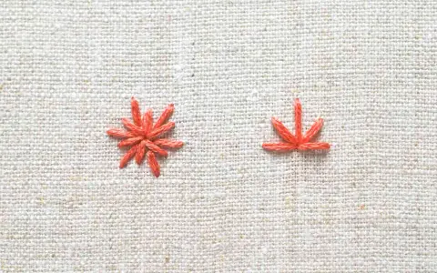 Two orange embroidery stitches on a textured linen fabric.