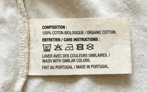 Etichetta con simboli tessuti: lavaggio 30°, non candeggiare, stirare a bassa temperatura, non lavare a secco, non asciugare in asciugatrice. 100% cotone biologico, fatto in Portogallo.