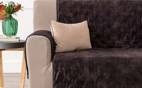 Divano con copridivano trapuntato marrone scuro, un cuscino beige e un vaso di fiori. Il miglior tessuto per divani per un look accogliente.