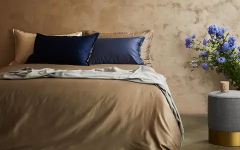 Letto con lenzuola color tabacco, cuscini blu e beige, coperta grigia. Il miglior tessuto per lenzuola per un sonno di qualità.