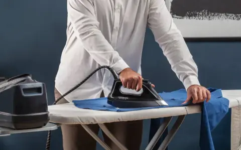 Uomo con camicia bianca che stira i panni su un asse da stiro, con un ferro a vapore e una caldaia Rowenta.