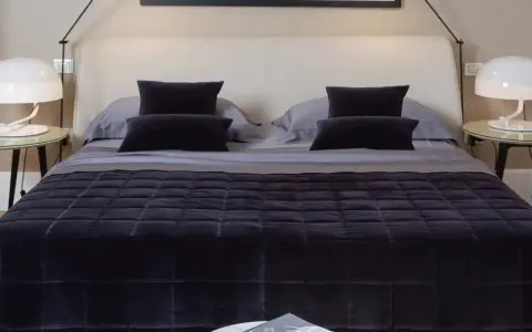 Un letto impeccabile, con copriletto trapuntato scuro e cuscini coordinati, mostra come rifare il letto in modo elegante.