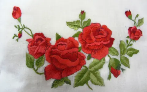 Ricamo di rose rosse su tessuto bianco, un delicato punto pittura che evoca un giardino fiorito.