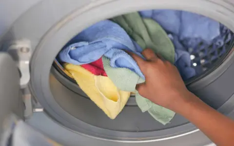 Mano inserisce asciugamani colorati in lavatrice. Scopri come lavare asciugamani in lavatrice per mantenerli morbidi e profumati.