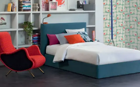 Letto una piazza e mezza con testiera blu, cuscini colorati e una poltrona rossa vivace.