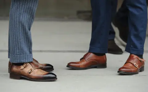 Primo piano su scarpe monk strap marroni e diversi tipi di orlo pantaloni: a risvolto e con pinces.