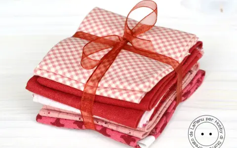Fazzoletti di stoffa rossi e rosa, con fantasie a quadretti e cuoricini, legati da un nastro. Perfetti per un progetto di cucito creativo.