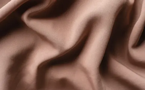 Tessuto di raso color tortora, morbido e drappeggiato, che mostra la sua texture fine. Il raso si può stirare per ottenere una finitura impeccabile.