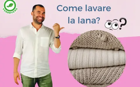 Uomo sorridente indica come lavare lana a mano. Pile di maglioni in primo piano.