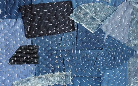 Tessuto patchwork in denim con cuciture bianche a punto croce e a zig-zag, un esempio di rammendo giapponese.