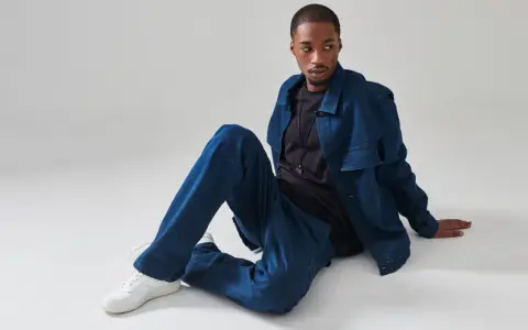 Un uomo con un completo di jeans blu, seduto a terra. Chissà quanto pesa un paio di jeans così comodi.
