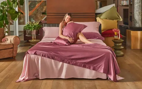 Donna sorridente su un letto con lenzuola rosa. Scopri come lavare le lenzuola nuove per mantenerle morbide e fresche.