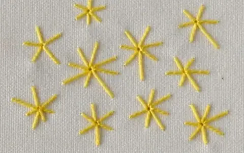 Piccole stelle gialle ricamate a punto pieno su tessuto bianco. Un esempio di come ricamare una stella a punto pieno.