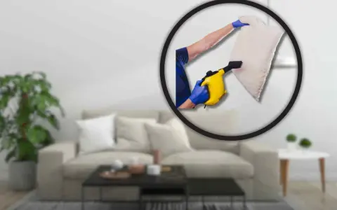 Pulizia profonda del divano per eliminare gli acari. Un braccio con guanto blu usa un pulitore a vapore giallo su un cuscino.