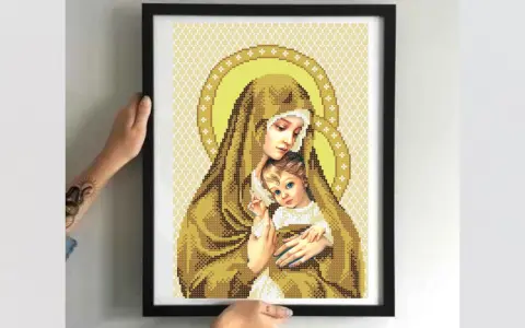 Cross-stitch of Madonna and Child in a black frame, held by hands.