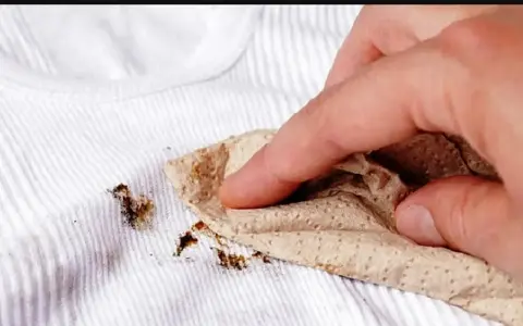 Dita che tamponano macchie marroni su biancheria antica con un tovagliolo di carta.