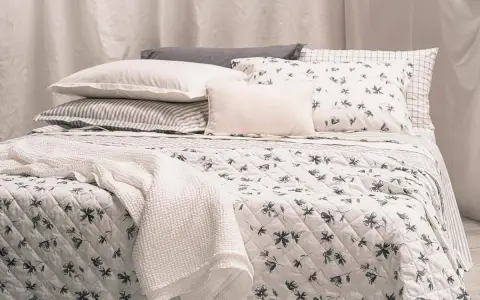 Un letto accogliente con biancheria a fiori e righe, coperte morbide e cuscini che invitano al riposo, come in un sogno di letti all'americana.