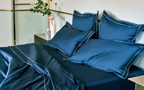 Letto matrimoniale con copriletto blu scuro e cuscini coordinati, rifiniti con bordi bianchi. Ideale per conoscere le misure copriletto matrimoniale.