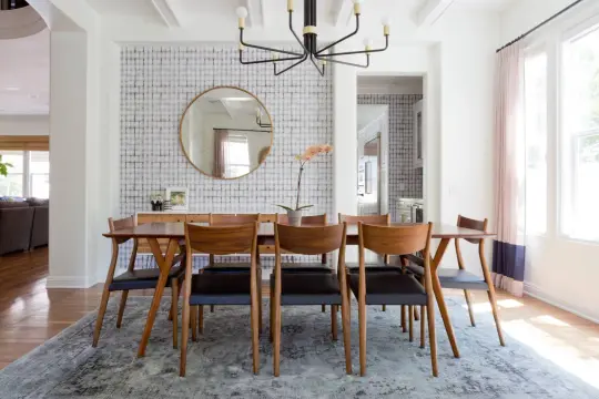 Tavolo da pranzo in legno con sedie in pelle nera, tappeto sotto il tavolo da pranzo si, con carta da parati a motivi geometrici e specchio rotondo.