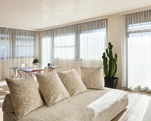 Soggiorno luminoso con divano beige e tende che non fanno vedere dall'esterno, creando un'atmosfera intima.