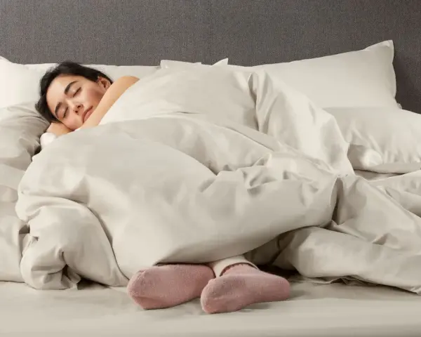 Donna dorme avvolta in lenzuola in microfibra che sembrano farla sudare, con solo i piedi in calzini rosa visibili.