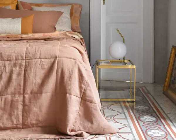 Un morbido quilt matrimoniale color pesca, con cuciture a quadri, adorna un letto in una stanza elegante.