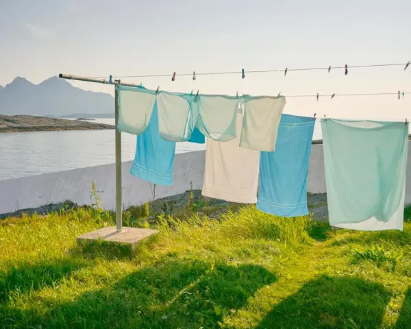 Magliette stese al sole su un filo, con montagne e mare sullo sfondo. Un modo naturale per stendere le magliette per non stirarle.