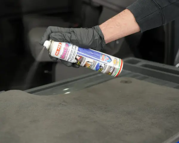 Mano con guanto nero spruzza spray Idrostop su tessuto grigio per impermeabilizzare.