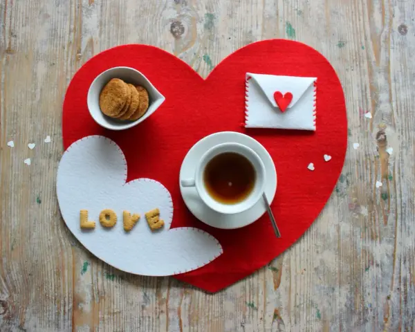 Tovagliette colazione fai da te a forma di cuore, con biscotti, tè e una busta decorata.