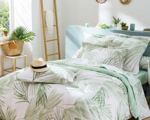 Un letto preparato per l'estate con biancheria a tema tropicale, un cappello di paglia e una borsa di vimini.