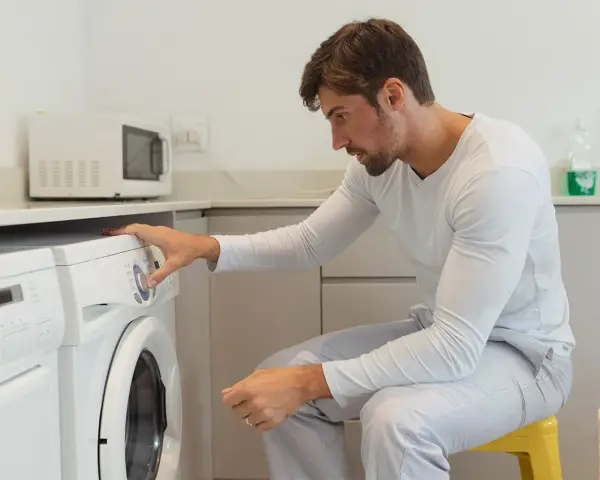 Uomo in pigiama imposta la lavatrice per asciugare la ciniglia.
