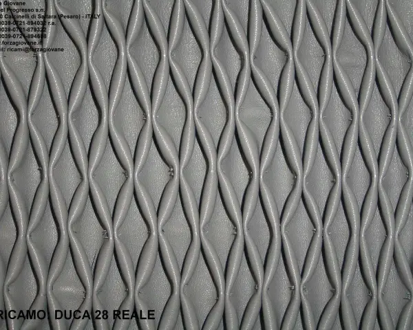 Ricamo in pelle grigia con un motivo a nido d'ape, che crea un effetto tridimensionale e geometrico.