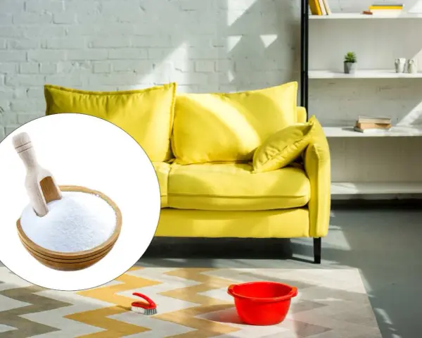 A bowl of baking soda with a scoop, next to a yellow sofa and cleaning supplies.