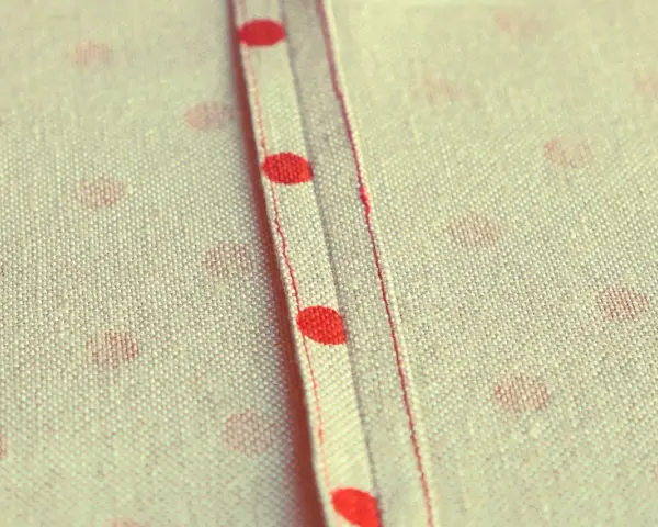 Tessuto a pois rossi con cucitura a vista, un punto per rifinire bordi con precisione sartoriale.