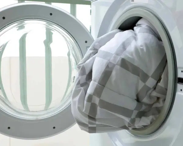 A white and grey checkered duvet being loaded into a washing machine.