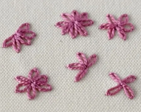 Close-up of five small, pink embroidered daisy stitches on a cream fabric background.