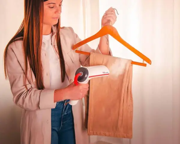 Donna usa un vaporizzatore per stirare velocemente i pantaloni appesi a una gruccia.