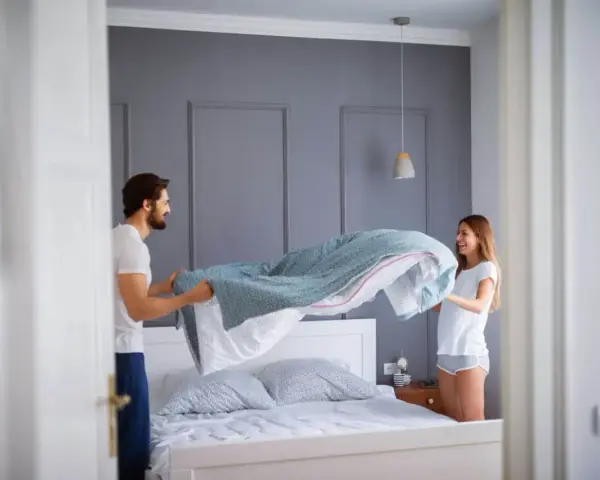 Coppia felice che cambia le lenzuola, un gesto che ci ricorda ogni quanto cambiare le lenzuola per un sonno più sano.