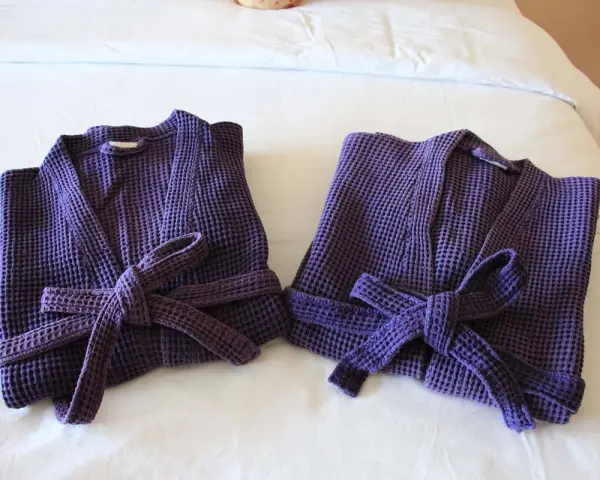 Due accappatoi viola, piegati e legati con la loro cintura, pronti per essere riposti. Ecco come piegare un accappatoio per un riordino perfetto.